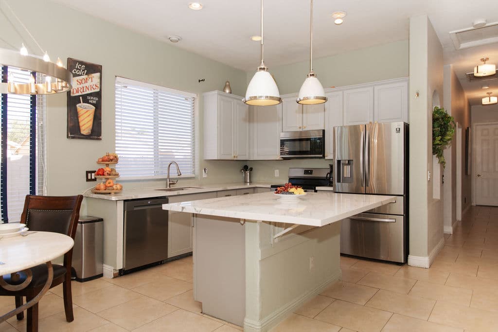 The bright Liora kitchen, with a marble-topped island, white cabinetry, stainless steel appliances and pendant lights.