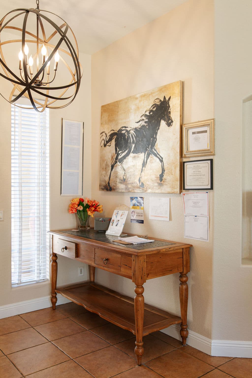 The entry hall inside the Liora home: a wooden console table with fresh flowers beneath a painting of a horse and an iron chandelier.
