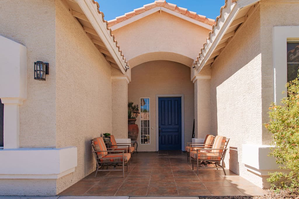 The covered front porch of the Liora home, with cushioned chairs on either side of a deep blue front door.