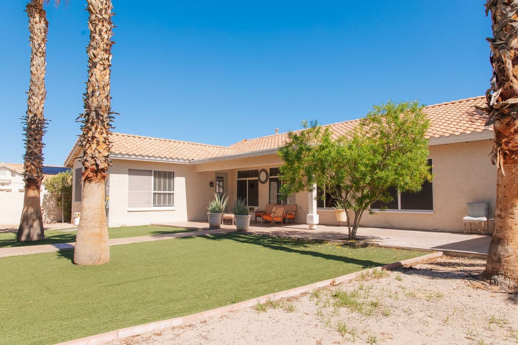 The back of the Liora home seen across a green lawn and palms, with the covered patio along the house.