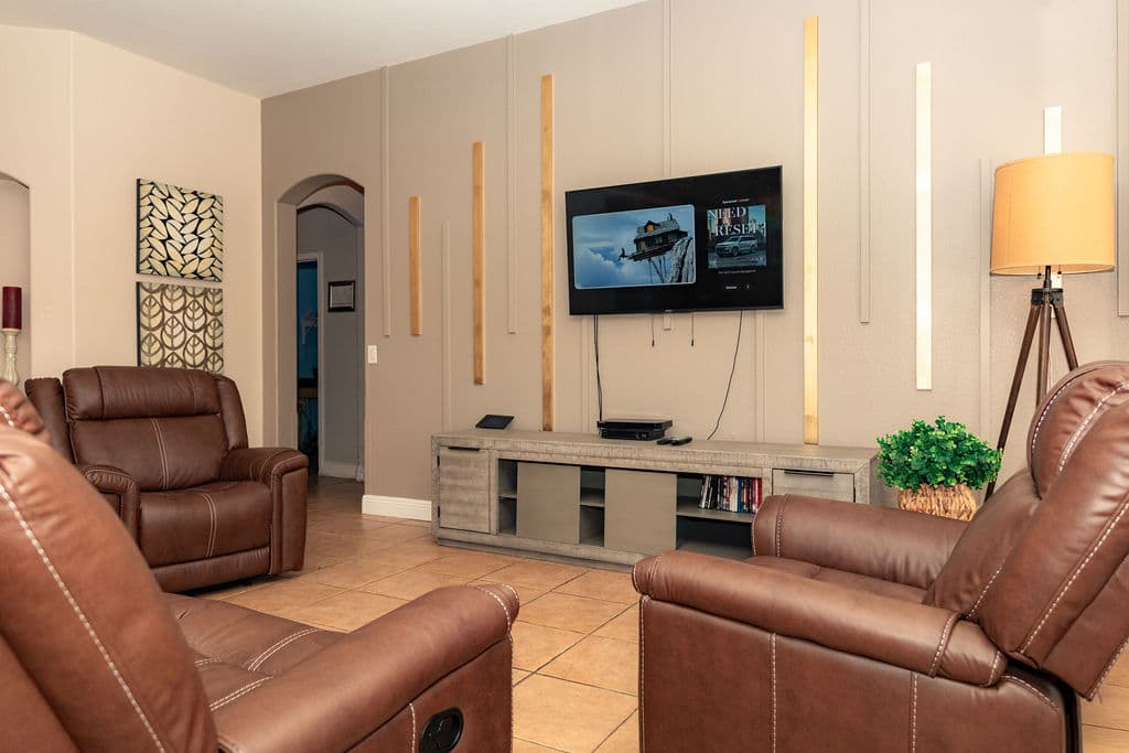 Another view of the living room, with recliners, a floor lamp, a potted plant and an arched doorway to the hall.