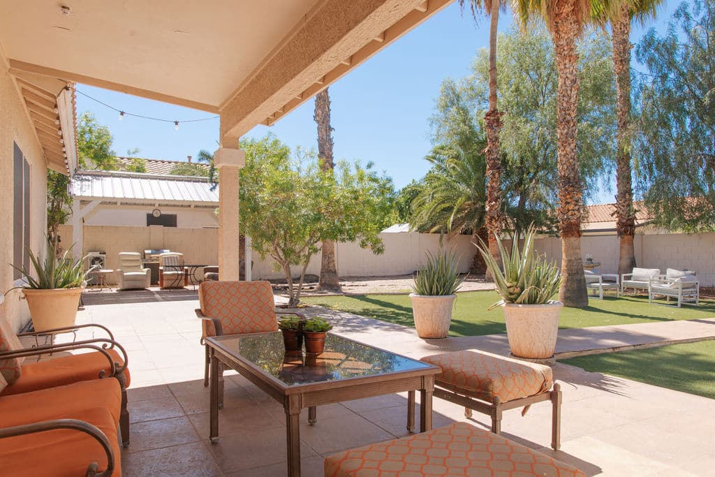 The covered back patio, with cushioned chairs around a glass table, potted agaves and a view across the lawn to the garden.